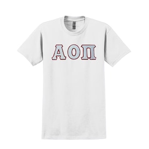 May include: White t-shirt featuring the Greek letters A, O, and Π in a light blue color with a maroon outline. The letters are centered on the front of the shirt. The shirt has short sleeves and a crew neck.