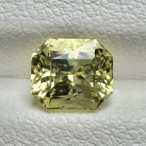 Könnte beinhalten: Ein facettierter, hellgelber Edelstein mit achteckiger Form. Der Stein hat einen Brillantschliff, der das Licht reflektiert und seine Klarheit zeigt. Die Farbe des Steins ist ein helles, warmes Gelb, vor einem neutralen Hintergrund.
