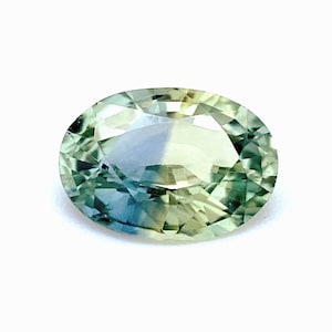 May include: An oval gemstone with a blend of green, blue, and yellow tones. The gem has a faceted surface that reflects light, creating a sparkling effect. The stone is set against a white background.
