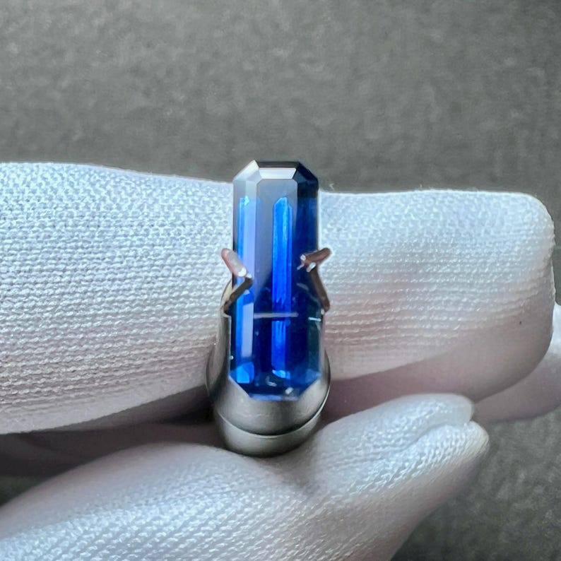 May include: A deep blue gemstone set in a silver ring setting. The gemstone is a rectangular shape with a faceted cut.