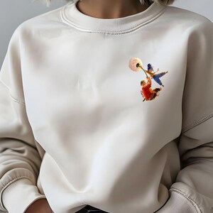 May include: A cream coloured sweatshirt with a graphic of two children holding onto a dandelion seed head. The children are wearing blue and red clothing.
