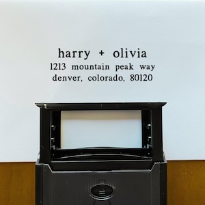 May include: A black rectangular stamp with the text "harry + olivia" and an address printed in black ink on a white background. The address includes the street name, city, state, and zip code.