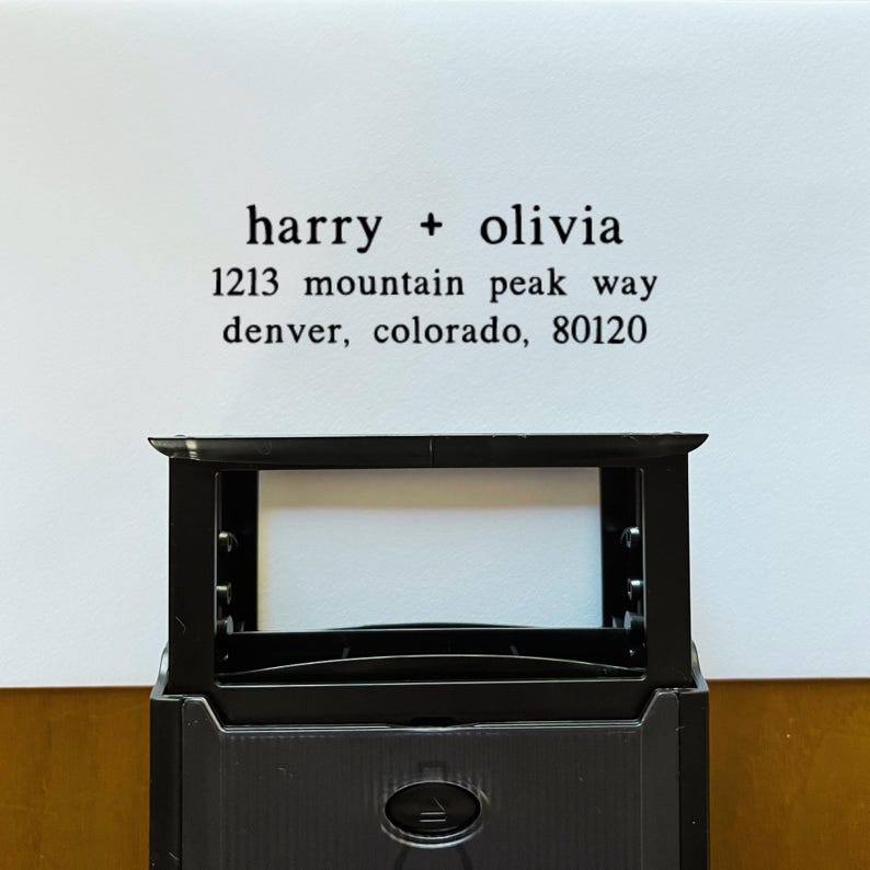 May include: A black rectangular stamp with the text "harry + olivia" and an address printed in black ink on a white background. The address includes the street name, city, state, and zip code.