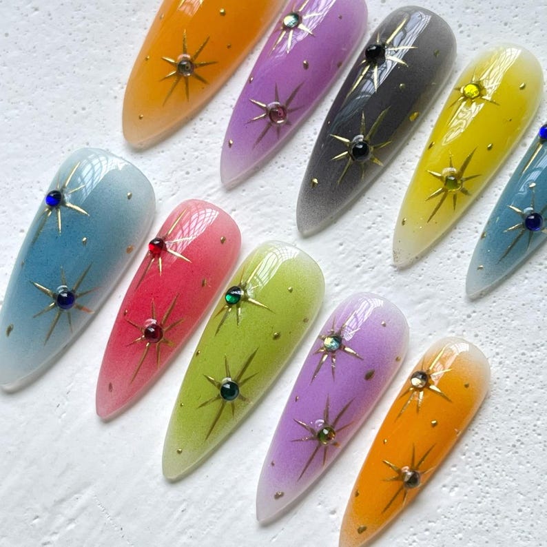 Puede incluir: Diez u&ntilde;as postizas largas y ovaladas con un efecto degradado ombr&eacute;. Cada u&ntilde;a est&aacute; pintada de un color diferente, incluyendo azul, rosa, verde, morado y amarillo. Cada u&ntilde;a tiene un dise&ntilde;o de estrella dorada con pedrer&iacute;a.