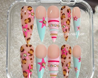 May include: A set of ten press-on nails in a clear plastic case, featuring almond and stiletto shapes. Designs include leopard print with pink stars and gold studs, light blue tips with pink stars, and pink stripes with rhinestones. Text reads Jade's nail bar.