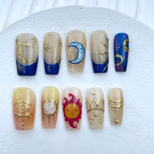 Puede incluir: Conjunto de diez uñas postizas con diseños celestiales. Las uñas son beige con detalles dorados y azules. Algunas uñas presentan lunas, estrellas, soles y ojos.