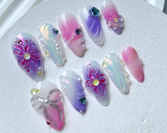 Può includere: Set di dieci unghie finte con una base bianco perlato e accenti iridescenti. Ogni unghia presenta un design diverso, tra cui fiori, fiocchi e vortici. Le unghie sono decorate con strass e perle.