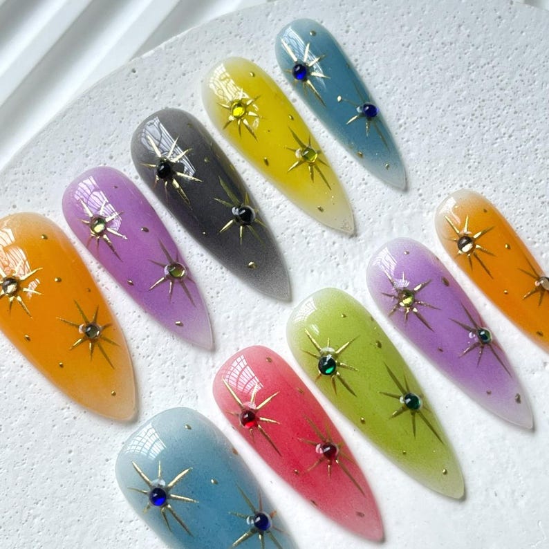Puede incluir: Un conjunto de diez u&ntilde;as postizas de colores con un dise&ntilde;o de estrella y pedrer&iacute;a. Las u&ntilde;as est&aacute;n dispuestas en un patr&oacute;n de arco&iacute;ris, con cada u&ntilde;a de un color diferente.