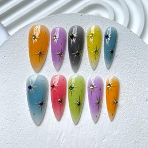 Puede incluir: Doce u&ntilde;as postizas largas y ovaladas con un efecto degradado ombr&eacute;. Cada u&ntilde;a tiene un dise&ntilde;o de estrella dorada y un solo strass en una variedad de colores.