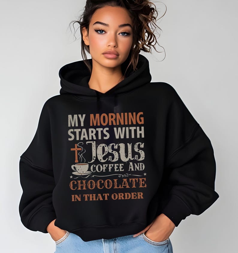 Peut inclure: Un sweat &agrave; capuche noir avec l'inscription "MY MORNING STARTS WITH Jesus COFFEE AND CHOCOLATE IN THAT ORDER" en blanc, orange et marron. Le motif comprend une croix, une tasse &agrave; caf&eacute; et des &eacute;toiles.