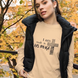 Könnte beinhalten: Ein beiges Langarmshirt mit dem Text "I am made in HIS IMAGE" und einer Fingerabdruck-Kreuzgrafik.