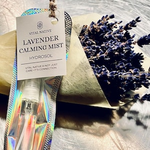 May include: A clear glass spray bottle of lavender calming mist with a white label that reads "Vital Native Lavender Calming Mist Hydrosol". A bundle of dried lavender is next to the bottle. The tag reads "Vital Native is not just care - it's connection."