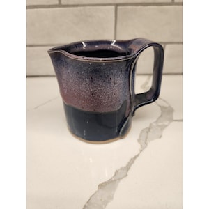 Puede incluir: Taza de cerámica hecha a mano con una forma orgánica única. La taza presenta una base azul oscuro, que transiciona a un medio rojo-púrpura y un borde azul oscuro. Tiene un asa grande y curvada para un agarre fácil.