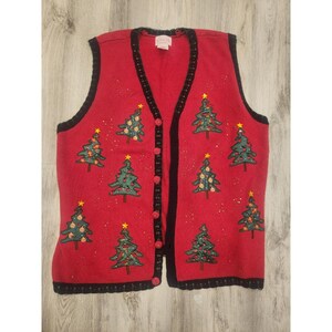 May include: A red knit vest featuring a V-neckline and a black trim along the edges. The vest is decorated with multiple embroidered green Christmas trees, each topped with a yellow star and adorned with small colorful ornaments and beads.