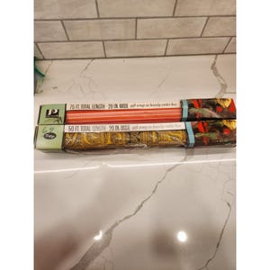 Könnte beinhalten: Zwei Geschenkpapierrollen in Kartons. Eine Schachtel hat rot-orange Streifen, die andere ein gold-schwarzes Muster. Beide Schachteln sind mit "75 FT. TOTAL LENGTH - 20 IN. WIDE" und "50 FT. TOTAL LENGTH - 20 IN. WIDE" beschriftet.