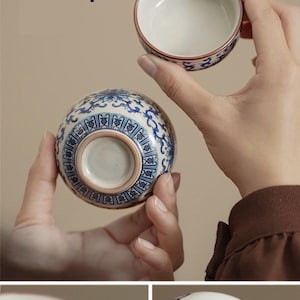 May include: Finely polished porcelain teacups. The teacups are white with blue floral patterns and a brown rim. One teacup is held upside down, showcasing the intricate design on the base. The text "Finely Polished Porcelain Teacups" is visible.