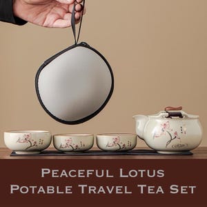 Puede incluir: Un juego de té portátil de color crema con una tetera y tres tazas a juego, todas adornadas con diseños de flores de loto rosas. El juego incluye un estuche de transporte y está etiquetado como "Peaceful Lotus Portable Travel Tea Set."
