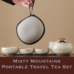 Puede incluir: Un juego de té portátil con una tetera, tres tazas y un estuche de transporte. El juego de té es de color blanquecino con un diseño de montaña. Las tazas y la tetera tienen un borde dorado. El estuche es gris con una cremallera negra.