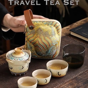 May include: A travel tea set with the text "FLYING APSARAS TRAVEL TEA SET". The set includes a patterned carrying case, a teapot, three small cups, and a glass. The cups and teapot have a cream base with a painted design.
