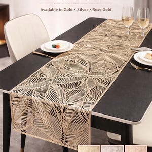 May include: A gold leaf-patterned table runner on a black table, with the text "Leaf Flow TABLE RUNNER" at the top. The runner is decorated with a repeating leaf design. Available in gold, silver, and rose gold.