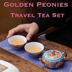以下が含まれることがあります： 「GOLDEN PEONIES TRAVEL TEA SET」の文字が入ったトラベルティーセット。 ティーポットと2つのティーカップが含まれており、すべて花柄のデザインです。 ティーポットには金色のハンドルと蓋が付いています。 ティーカップとティーポットは紫色のマットの上にあります。