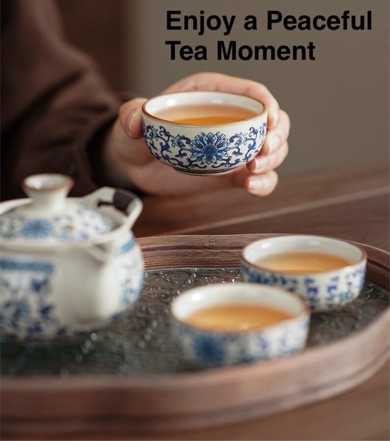 May include: A hand holding a small teacup filled with tea, with a blue and white floral design. The image includes a teapot and two other teacups on a tray. Text reads: "Enjoy a Peaceful Tea Moment."