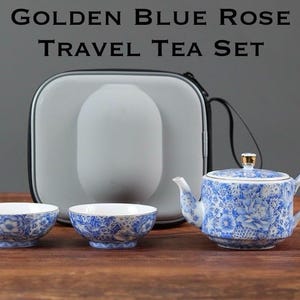 Peut inclure: Un service à thé de voyage Golden Blue Rose comprenant une théière, deux tasses et un étui de transport gris. La théière et les tasses présentent un motif floral bleu avec des bordures dorées. L'étui a une poignée noire.