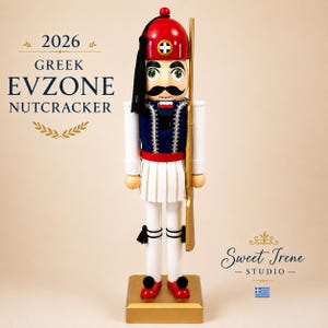 May include: A wooden nutcracker dressed as a Greek Evzone soldier, wearing a red fez with a black tassel, a blue vest with white trim, and a white pleated fustanella skirt. The figure holds a gold rifle and stands on a gold rectangular base.