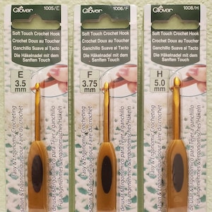 May include: Three Clover brand crochet hooks with gold-colored metal hooks and black handles. The hooks are labeled with sizes E 3.5 mm, F 3.75 mm, and H 5.0 mm. The packaging is green and white with the text "Soft Touch Crochet Hook" in multiple languages.
