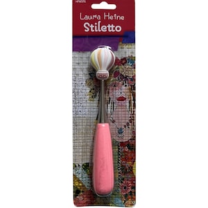 May include: A pink and silver stiletto tool with a hot air balloon design on the top. The packaging features the text "Laura Heine Stiletto" and a colorful floral pattern.