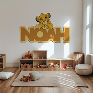 May include: A wall decal featuring the name "NOAH" in large, yellow letters, with a cartoon lion cub perched on top. The decal is in a child's room with wooden shelves and toys.
