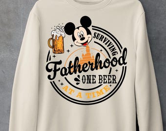 May include: A beige sweatshirt with a graphic print of Mickey Mouse holding a beer mug. The graphic also includes the text "Surviving Fatherhood One Beer At A Time".
