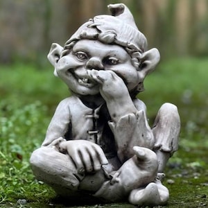 Puede incluir: Una estatua de gnomo de jardín de piedra gris con una sonrisa traviesa, sentado con una mano cubriéndose la boca y la otra descansando sobre su pierna.