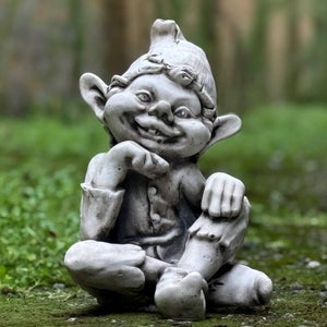 Puede incluir: Una escultura de gnomo de jardín de piedra gris sentada con una expresión pensativa. El gnomo lleva un sombrero puntiagudo y tiene una barba larga.