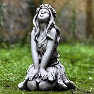 May include: A gray stone statue of a woman with a flower crown sitting with her hands clasped in her lap. She is looking up with a peaceful expression.