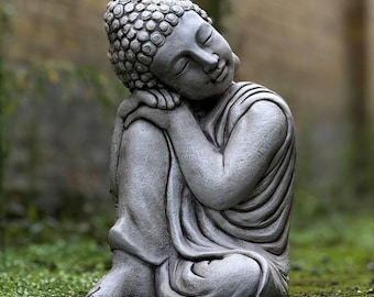 May include: A gray stone statue of a meditating Buddha, sitting with legs crossed and head resting on one hand. The statue is in a relaxed pose, with eyes closed and a serene expression.