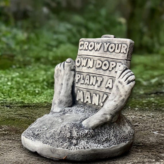 A chunky handmade concrete garden statue with a dry 'Grow Your Own Dope — Plant a Man' pun baked right into the stone — genuinely weird and wonderful patio decor.