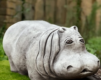 Puede incluir: Una escultura de piedra gris de un hipopótamo acostado. La escultura tiene una cara detallada con ojos grandes y una superficie texturizada.