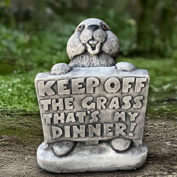 A handmade concrete bunny sculpture holding a 'Keep Off the Grass' sign — genuinely funny, tactile, and the kind of garden piece that makes visitors do a double-take.