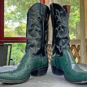 May include: A pair of green cowboy boots with black leather accents and intricate stitching. The boots have a pointed toe and a low heel.