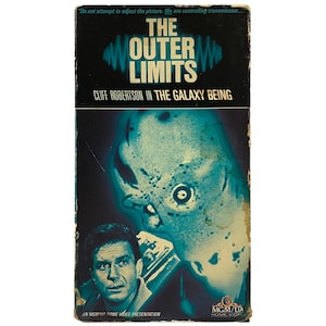 May include: A VHS tape cover for the science fiction television series "The Outer Limits". The cover features a close-up of a blue and green alien creature with a large eye. The text on the cover reads "The Outer Limits" and "Cliff Robertson in The Galaxy Being".