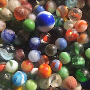 May include: A collection of colourful glass marbles in various sizes and patterns. The marbles are arranged in a random pattern, with some overlapping. The marbles are mostly opaque, with some clear or translucent marbles. The marbles are a mix of colours, including red, blue, green, yellow, and white.