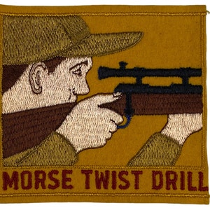 May include: A brown embroidered patch with a cartoon image of a person aiming a rifle with a scope. The text "MORSE TWIST DRILL" is printed in red below the image.
