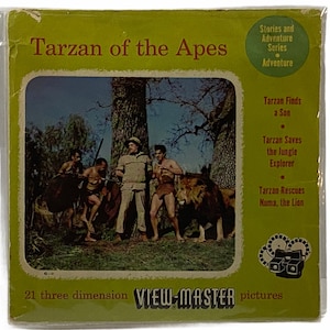 Puede incluir: Un carrete View-Master vintage con Tarzan de los monos. La parte delantera del carrete muestra una escena de la película con Tarzán, un león y otros personajes. El texto en el carrete dice "Tarzan of the Apes" y "21 three dimension VIEW-MASTER pictures".