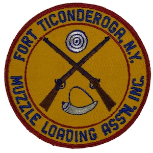 Puede incluir: Un parche circular amarillo y rojo con el texto "Fort Ticonderoga, N.Y. Muzzle Loading Assn. Inc." El parche presenta dos rifles cruzados, un blanco de tiro y un cuerno de pólvora.