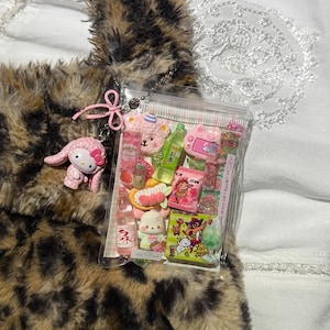 May include: A clear plastic pouch filled with miniature food and character charms, attached to a brown and black leopard print faux fur bag. A pink My Melody charm with a bow hangs from the pouch, which contains small replicas of drinks, snacks, and a bear face.