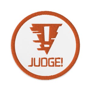 May include: Round embroidered patch with a white centre and an orange border. The centre features an orange exclamation mark design above the word "JUDGE!" in orange block letters.
