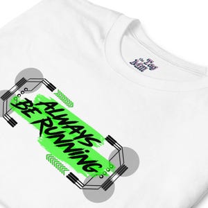 Puede incluir: Camiseta blanca con el texto "ALWAYS BE RUNNING" en negro y verde neón. El diseño incluye formas geométricas y flechas. El logotipo de Tag Mill es visible en el cuello.