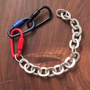 May include: A silver chain bracelet with a black, blue, and red carabiner clip attached.