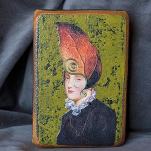 May include: A painting of a woman wearing a hat made of a large, orange and red leaf. The background is a green, textured surface.